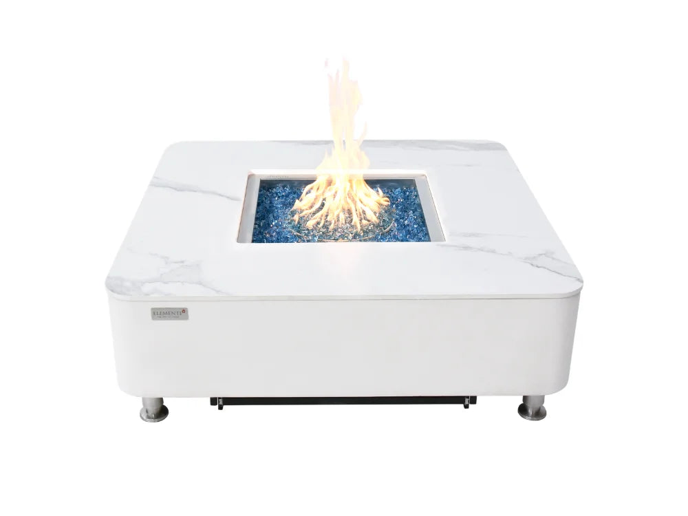 Elementi Marble square Cream white outdoor fire pit table with a faux-marble pattern, featuring a central firebox filled with blue glass rocks and a glowing yellow flame, shown on a solid white background.