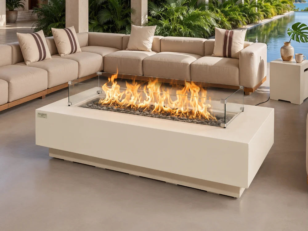 Elementi modern rectangular outdoor fire pit table with a glass wind guard and active flames, positioned in front of a beige sectional sofa on a patio.
