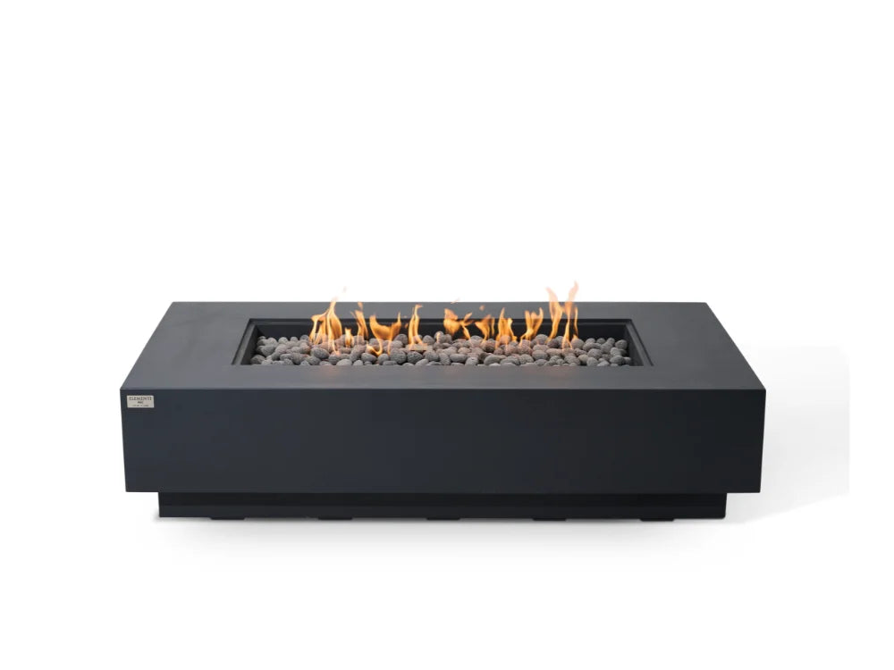 Elementi rectangular dark gray outdoor fire pit table with a modern design, featuring a glowing orange flame and gray stones inside, set against a plain white background.